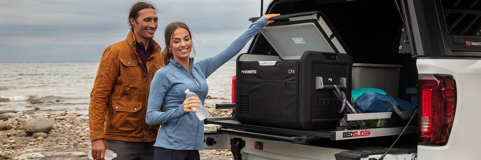 A Man and Women Off Road By the Water Opening a Cooler in the back of a GMC Vehicle