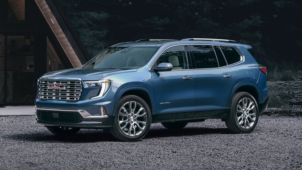 Front Three-Quarters View of the GMC Acadia Mid-Size SUV Parked Near a Cabin