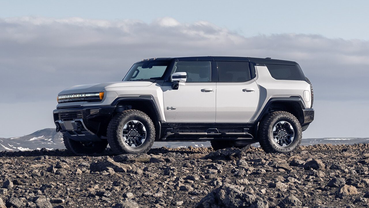 Profile View of a White GMC HUMMER EV SUV Parked on Rough Terrain Near Snow Covered Mountains