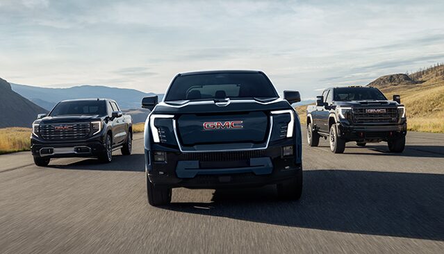 Front View of Three GMC Pickup Trucks Driving Down an Open Road