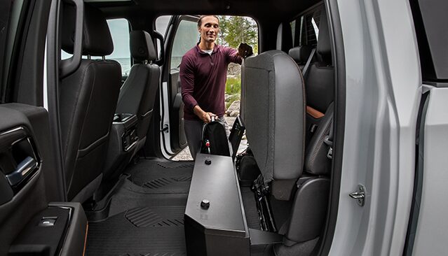 A Man Demonstrating the Spacious Interior of a GMC Truck with Folded Rear Seats and an Under-Seat Storage Compartment