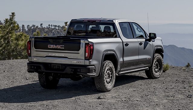 A Rear View of a Gray GMC Sierra AT4X Truck Parked on a Gravel Trail Overlooking a Mountainous Landscape