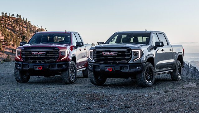 A Red GMC Sierra HD AT4X and a Gray GMC Sierra HD AT4X Truck Parked on a Dirt Trail in a Mountain Setting