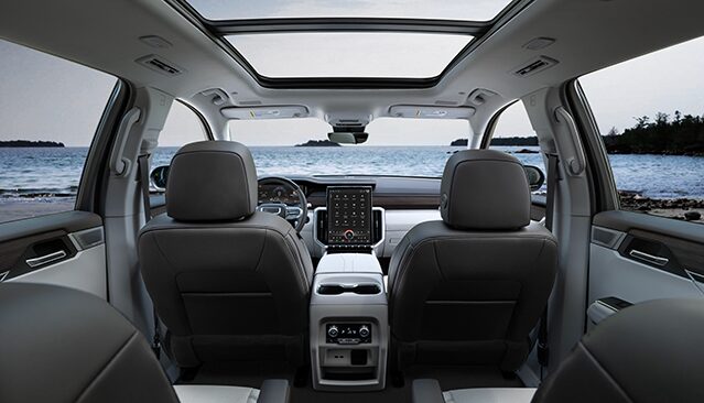 The Interior View of a GMC Vehicle's Rear Passenger Seats Looking Forward, with a Panoramic Sunroof and the Ocean Visible Through the Windshield