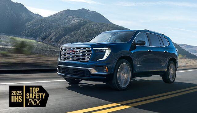A Blue GMC Acadia SUV Driving on a Winding Road with Mountains in the Background and a 2025 IIHS Top Safety Pick Badge
