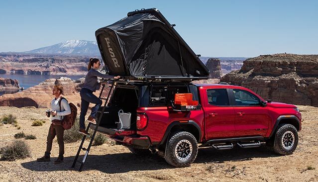 A Red GMC Canyon Pickup Truck with a Rooftop Tent and Camping Gear, with Two People by the Truck