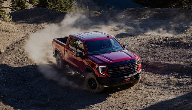 A Red GMC Sierra AT4X Pickup Truck Driving Off-Road on a Dusty Trail With Mountains in the Background