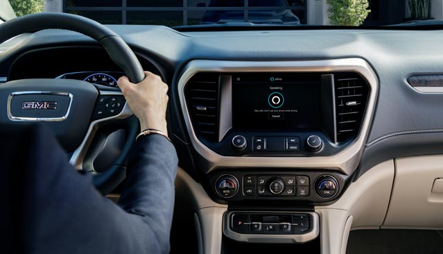 A Person's Hands on the Steering Wheel of a GMC Vehicle With the Infotainment Screen Showing a Voice Assistant