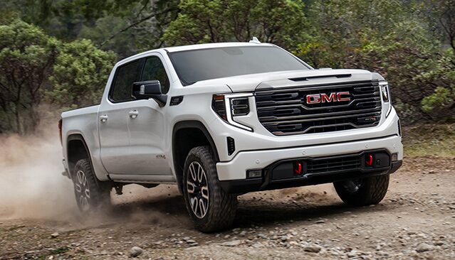 A White GMC Sierra AT4X Truck Driving on a Dirt Road Kicking Up Dust in a Natural Tree-Lined Environment