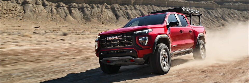 A Red 2025 GMC Canyon AT4 Driving Off-Road Kicking Up Dirt