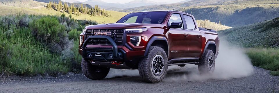 A Three-quarter View of a Red 2025 GMC Canyon AT4 Off-roading on a Rocky Trail