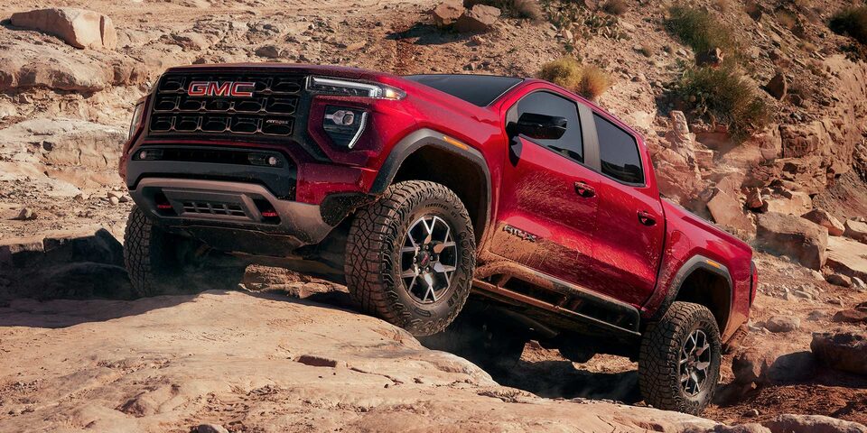 A Red 2025 GMC Canyon AT4 Driving Uphill Off-Road on Rocks