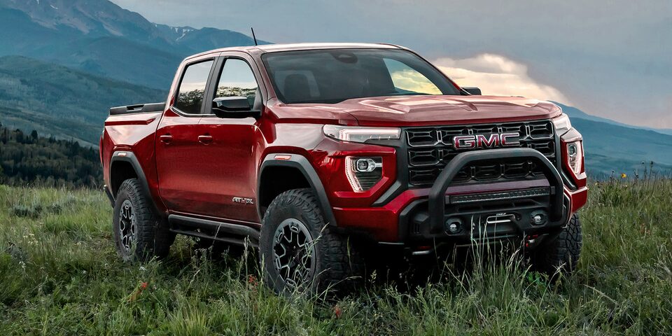 Three-quarter View of a Red 2025 GMC Canyon AT4 Parked in a Grassy Field