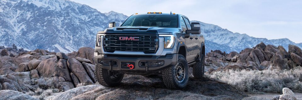 Wide Front Three-Quarters View of a 2025 GMC Sierra HD AT4 Truck Parked in Front of Snow-Covered Mountains