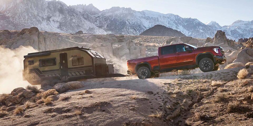 Side View of a 2025 GMC Sierra HD AT4 Truck Hauling a Small Trailer Through the Mountains