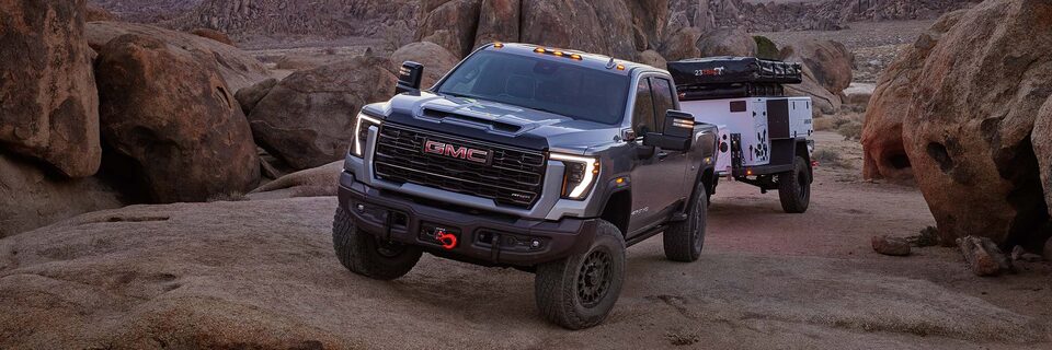 Wide View of a 2025 GMC Sierra HD AT4 Truck Hauling a Trailer Through Rocky Terrain at Dusk