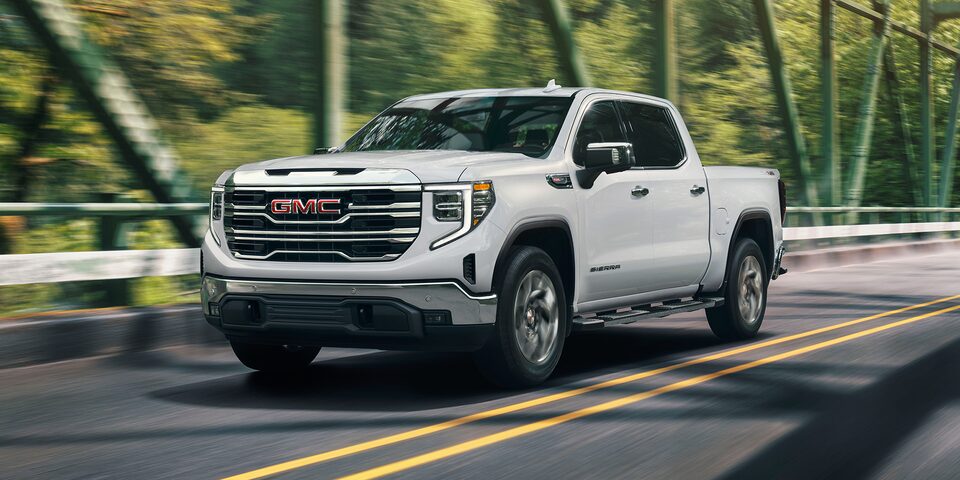 Front Three-Quarters View of a White Sierra Pickup Truck Driving Down the Road