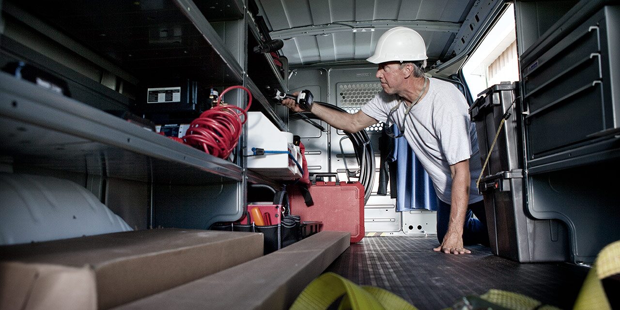 Interior View of a 2026 GMC Savana Cargo Van as a Worker in a Hard Hat Reaches for Tools