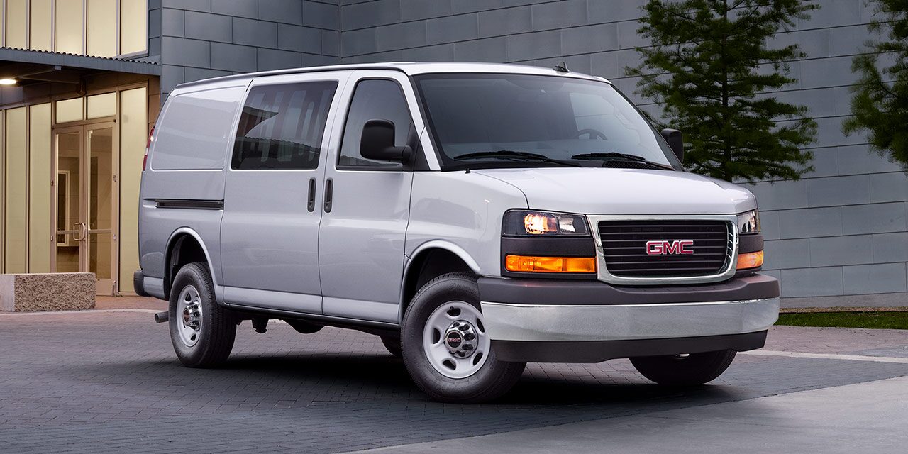 A Silver 2026 GMC Savana Cargo Van Parked on a Paved Area in Front of a Modern Building