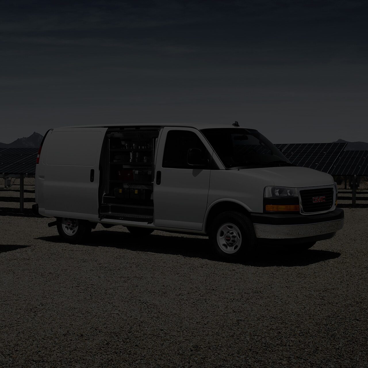 A White 2026 GMC Savana Cargo Van with its Side Door Open, Revealing Interior Shelving, near Solar Panels