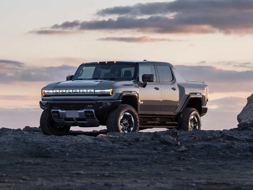 Front Three-Quarters View of the GMC HUMMER EV Pickup Truck Parked on Top of a Rocky Mountain at Sunset
