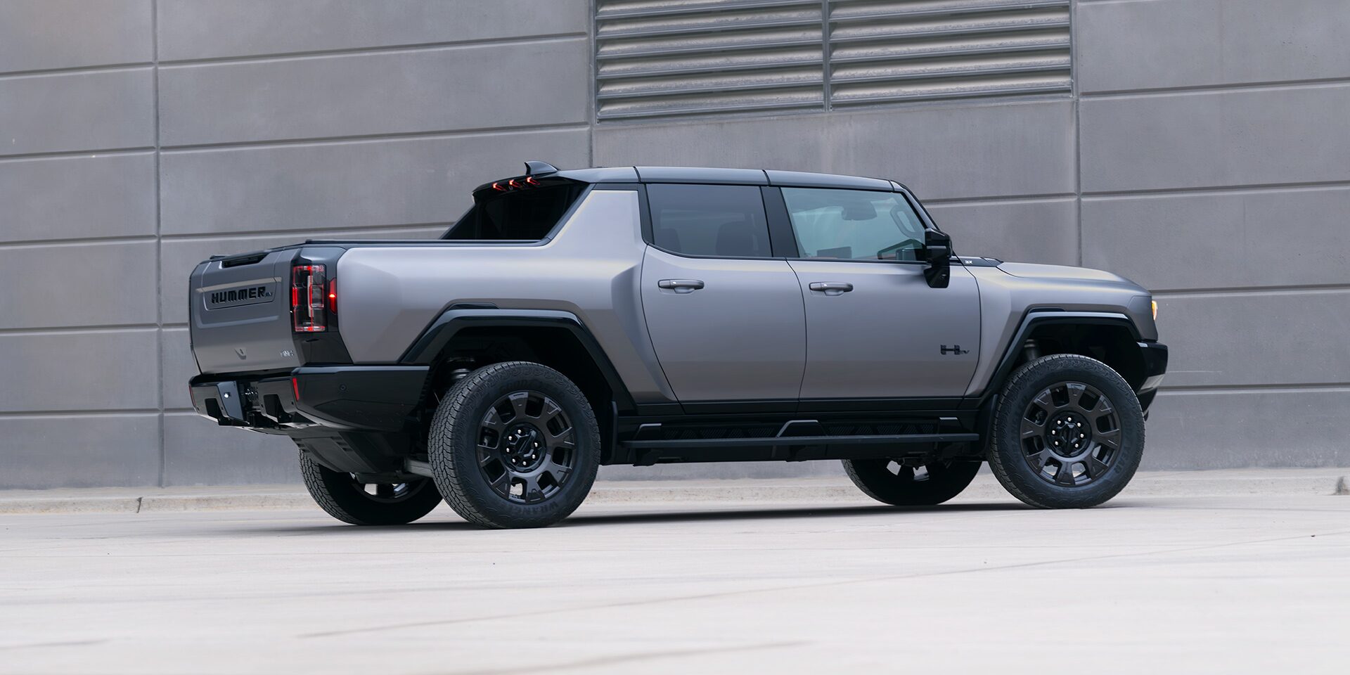 Rear Passenger Side View of the GMC HUMMER EV Pickup Truck Parked by a Concrete Wall