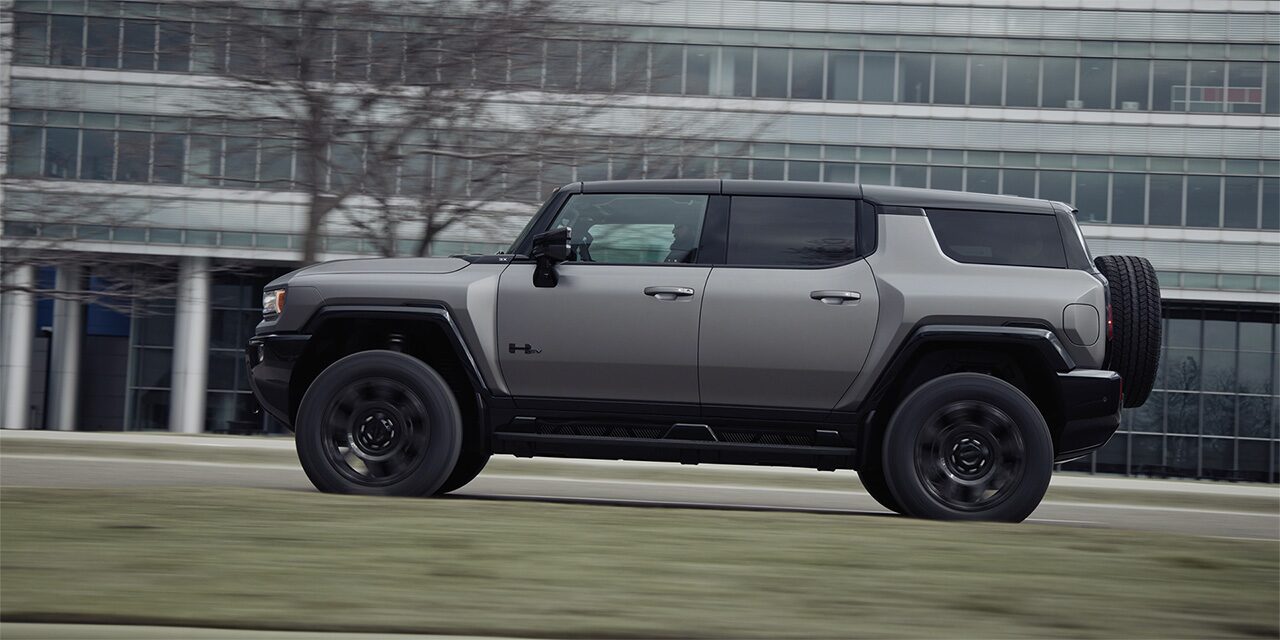 Blurry Driver Side View of the 2026 GMC HUMMER EV SUV Driving Past a Building