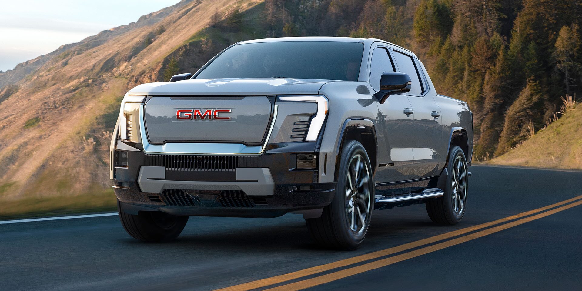 Three-quarters View of a 2026 GMC Sierra EV Pickup Truck Driving Through a Mountain Road