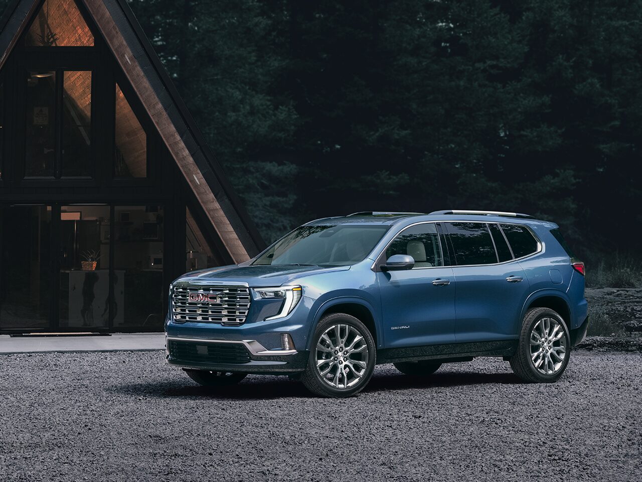 Front Three-Quarters View of the GMC Acadia Denali Luxury Mid-Size SUV Parked In Front of a Modern Cabin