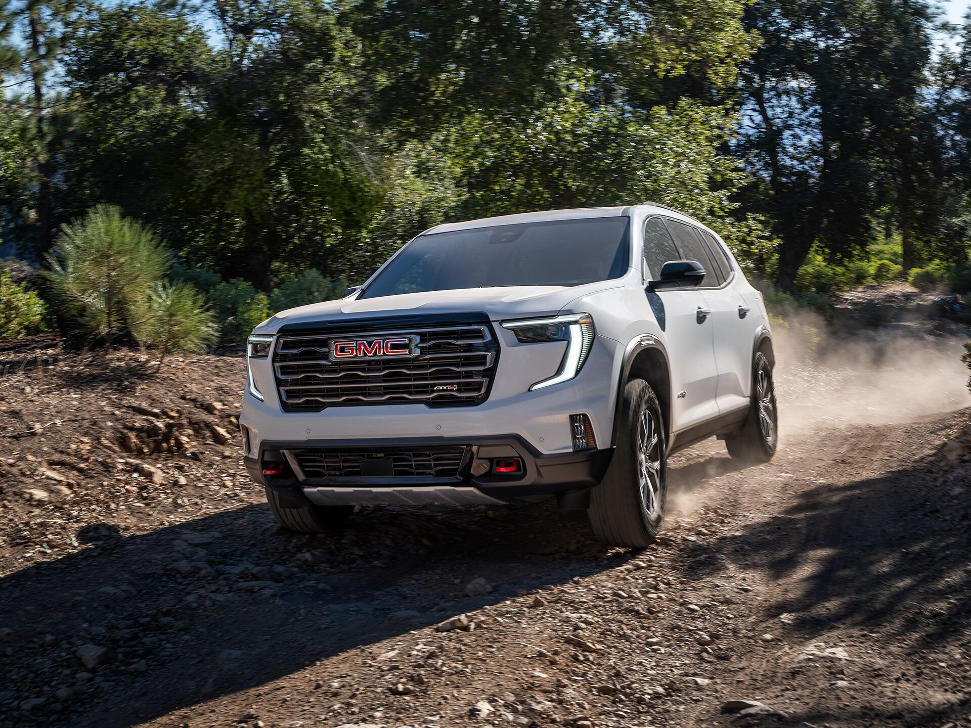 A White 2026 GMC Acadia Mid-Size SUV Parked Driving Down a Dirt Path Between Trees