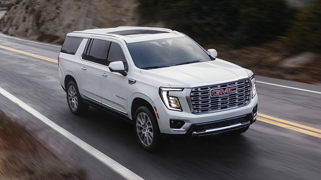 Front Three-Quarter View of the 2026 GMC Yukon Large SUV Driving Down a Mountain Lined Road
