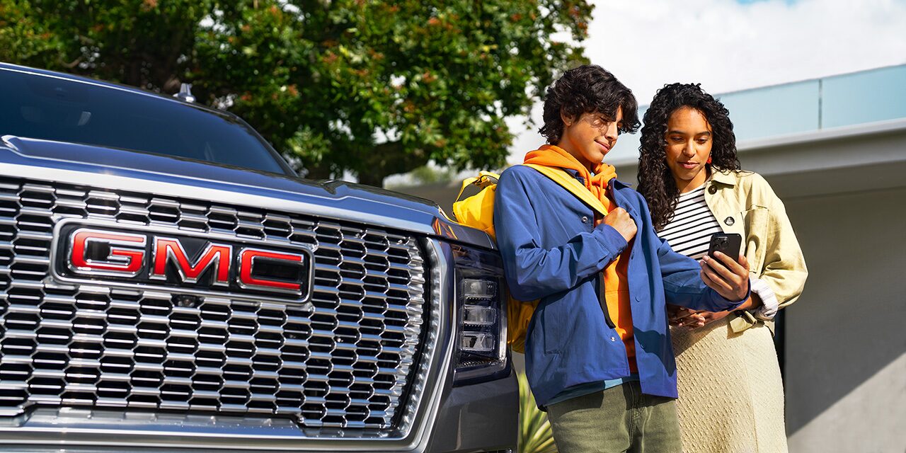 A Couple Standing in Front of Their GMC Yukon While They Use Their Smartphone