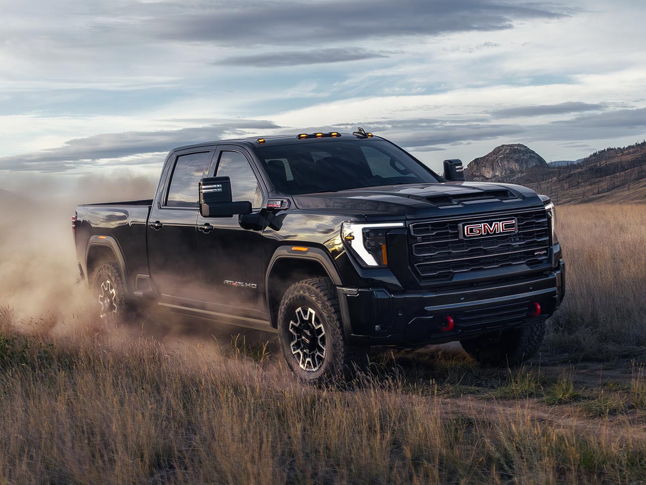 Front Three-Quarter View of the 2026 GMC Sierra HD Heavy Duty Truck Driving Down a Dirt Road
