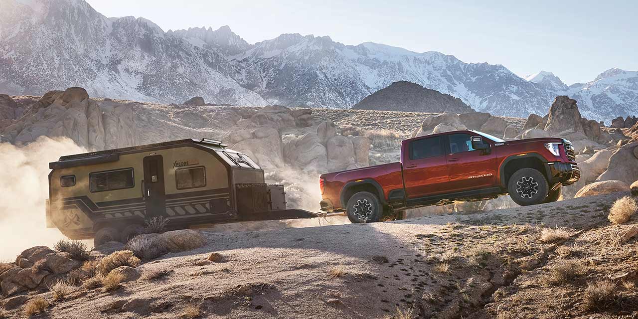 Profile View of the 2026 GMC Sierra HD Heavy Duty Truck Hauling a Trailer on a Rocky Mountain Road