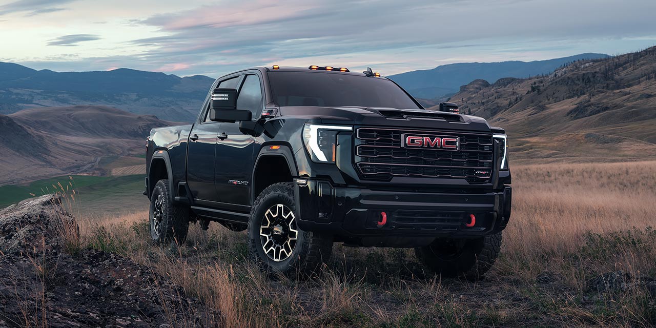 Front Three-Quarters View of a 2026 GMC Sierra HD Parked on a Terrain Field Surrounded by Mountains
