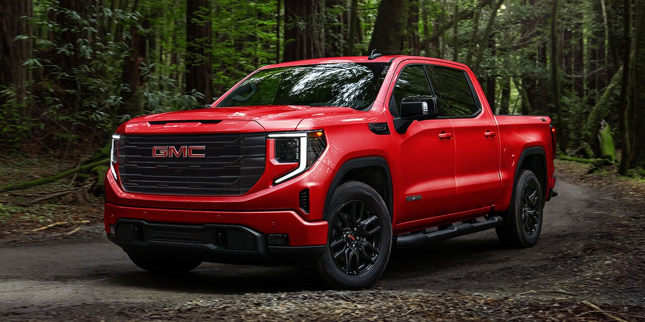 Front Three-Quarters View of a Red 2026 GMC Sierra 1500 Pickup Truck Parked in a Green Forest