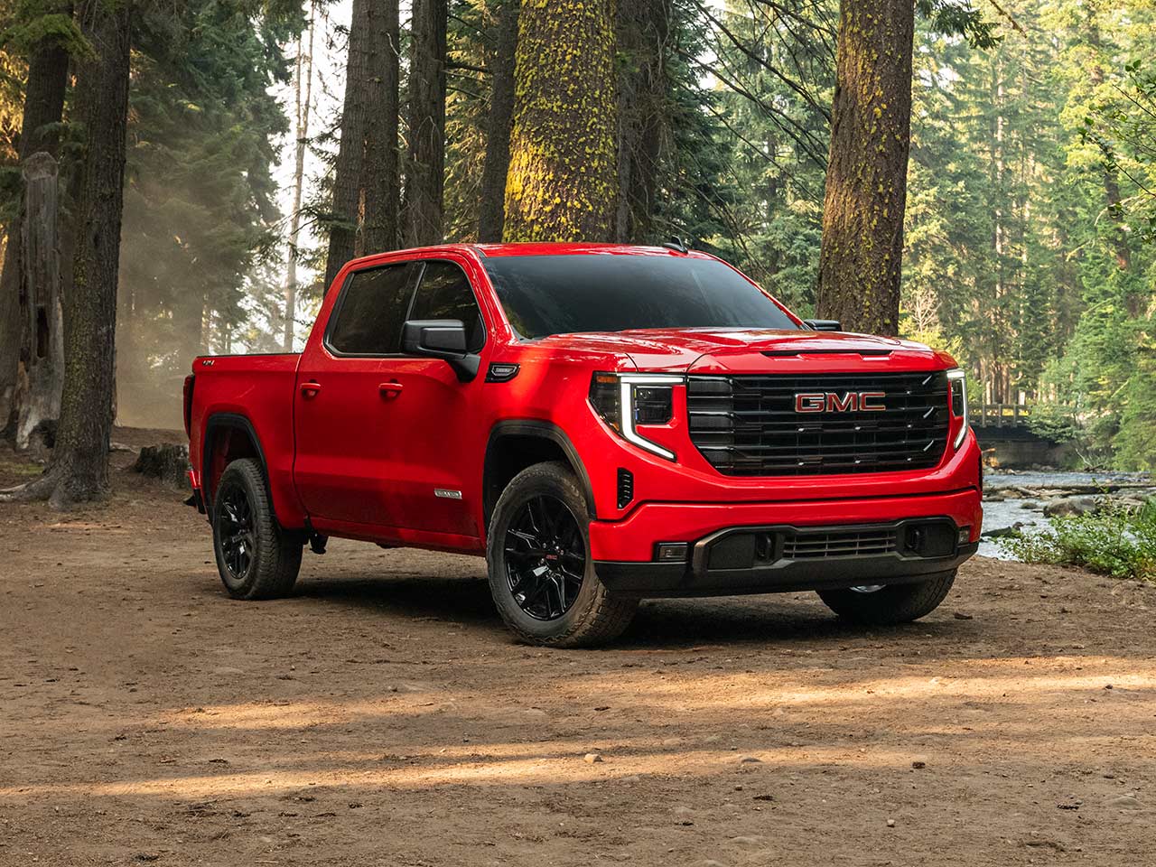 Front Three-Quarters View of a Red 2026 GMC Sierra 1500 Pickup Truck Parked in a Forest