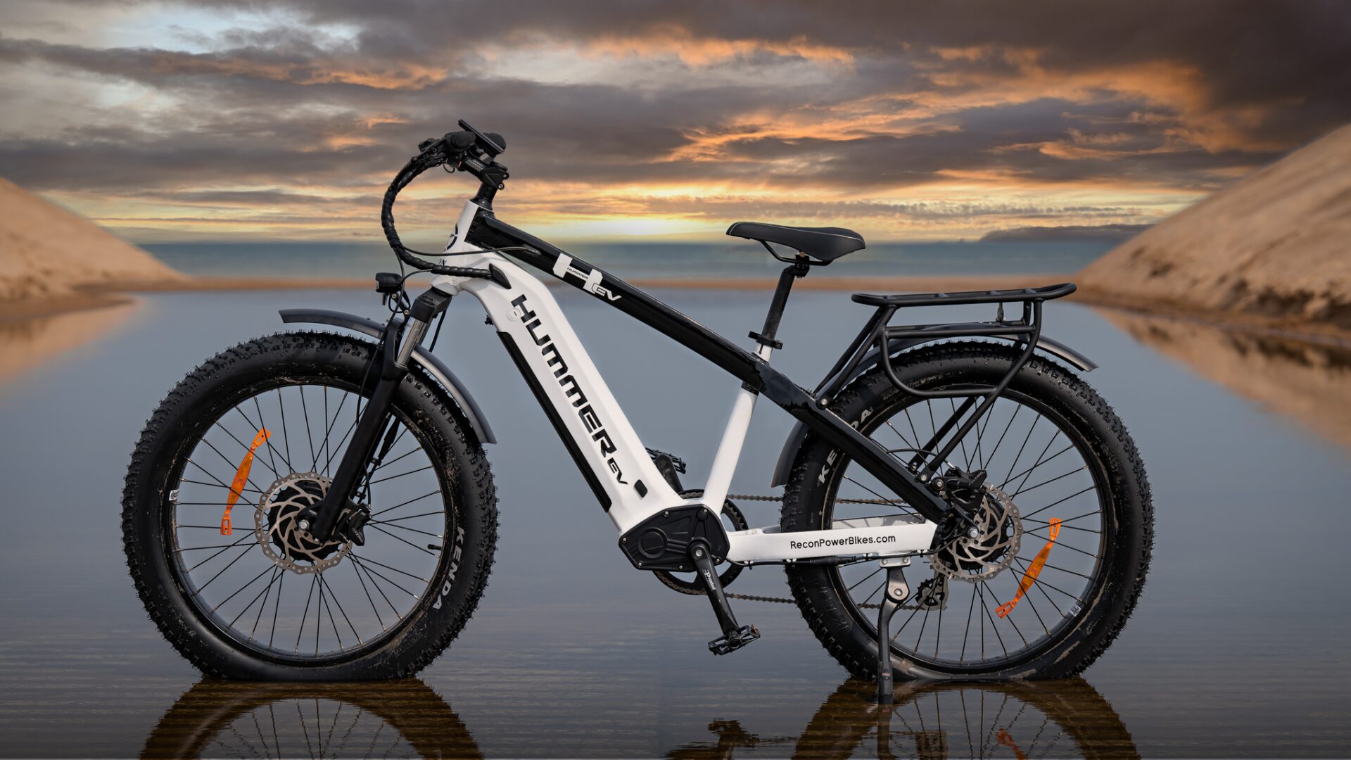 Side View of the AWD Electric Bike Parked on the Beach in a Puddle of Water with a Colorful Sunset View in the Background